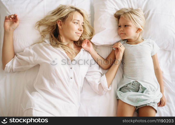 Cheerful mother and child lying on the bed at home, top view. Parent feeling, togetherness, happy times. Mother and child lying on the bed, top view