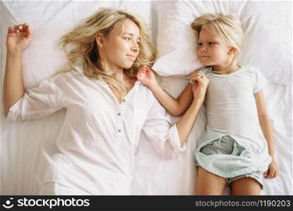Cheerful mother and child lying on the bed at home, top view. Parent feeling, togetherness, happy times. Mother and child lying on the bed, top view