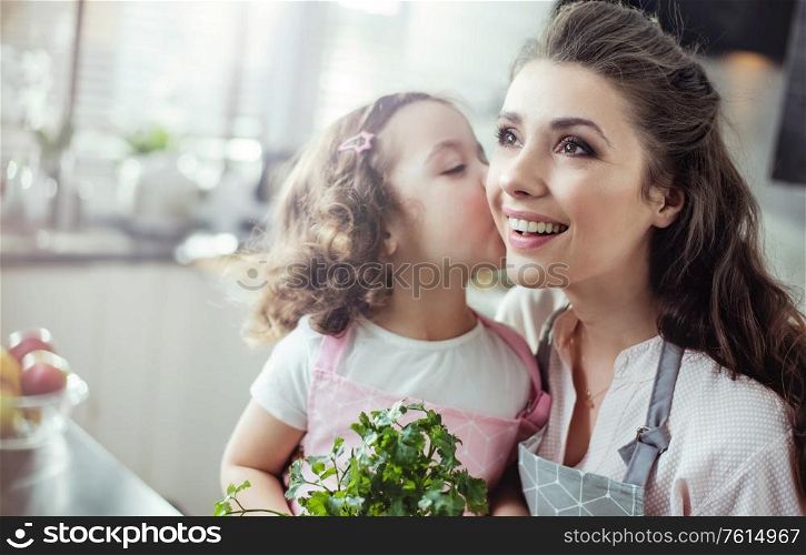 Cheerful mother and daughter holding herbs - kitchen shot