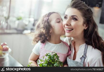 Cheerful mother and daughter holding herbs - kitchen shot