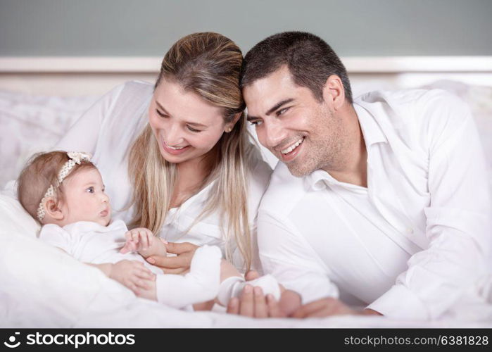 Cheerful mother and father playing with their cute baby daughter, with pleasure spending time together at home, happy young family