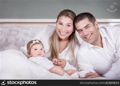 Cheerful mother and father playing with their cute baby daughter, with pleasure spending time together at home, happy young family