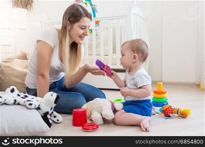 Cheerful mother and her baby boy on floor playing with toys