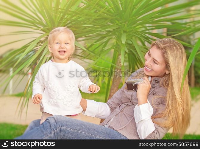 Cheerful mother taking picture of her cute little daughter in the park, happy young family having fun outdoors, parental love and enjoyment