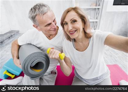 cheerful old couple taking self portrait holding yoga mat dumbbells hand