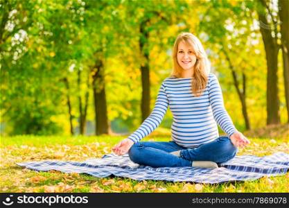 cheerful pregnant woman in the park sitting in the lotus position