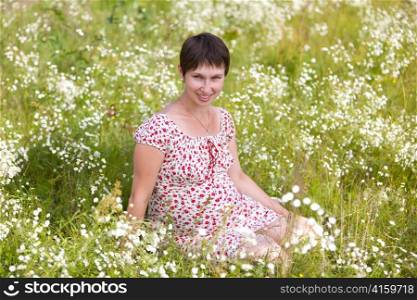 Cheerful pregnant woman sitting in chamomile background
