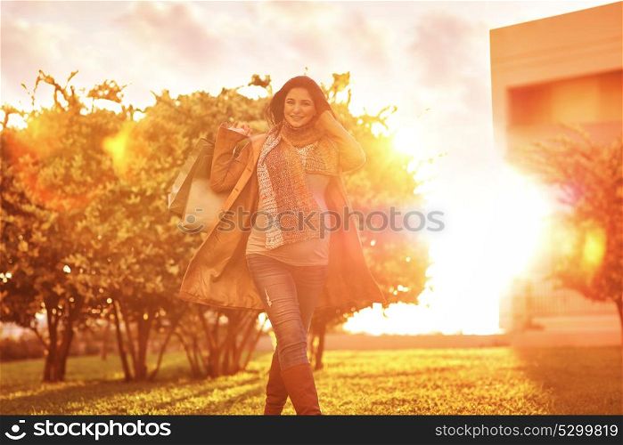 Cheerful pregnant woman with shopping bags in the garden in bright sunny day, autumn season sale, doing purchase for a baby, happy pregnancy period