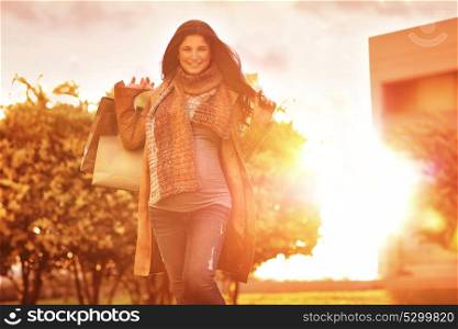 Cheerful pregnant woman with shopping bags in the garden in bright sunny day, autumn season sale, doing purchase for a baby, happy pregnancy period