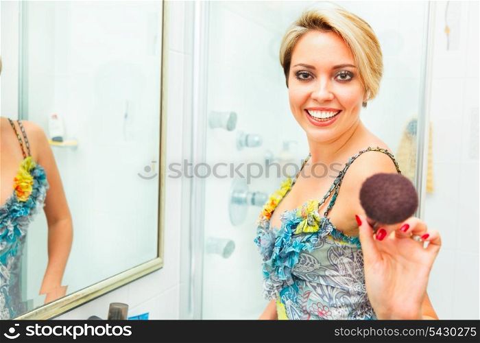 Cheerful pretty young woman in bathroom extends fluffy brush in camera&#xA;