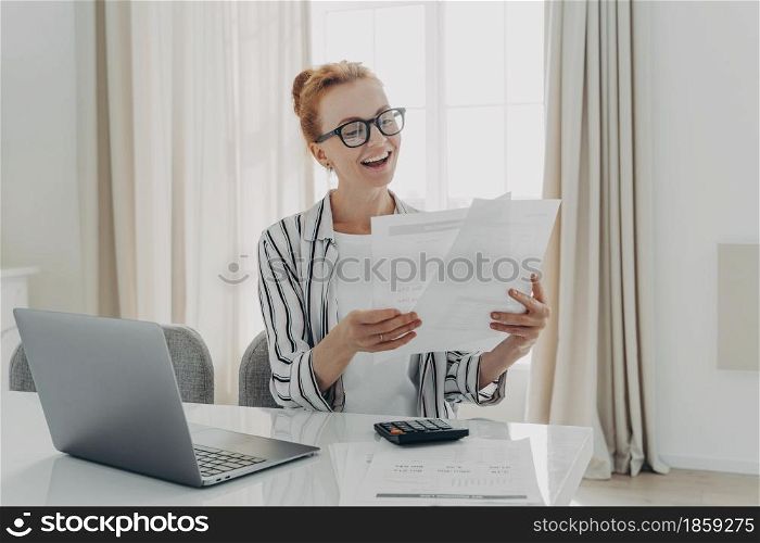 Cheerful professional accountant prepares annual financial report checks results looks at documents counts tax rateson calculator manages family budget pays bills on laptop computer. Savings concept. Cheerful professional accountant prepares annual financial report looks at documents