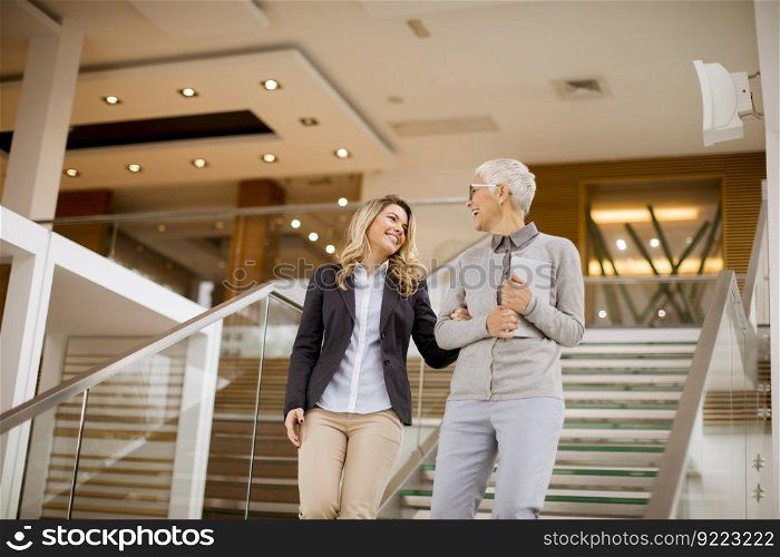 Cheerful senior and young businesswomen getting down the stairs in modern office