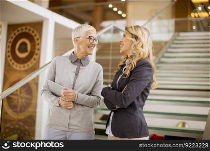 Cheerful senior and young businesswomen getting down the stairs in modern office