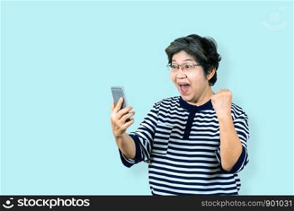 Cheerful senior asian woman holding and looking smartphone on isolated background feeling win ,celebrating and victory. Older female lifestyle concept blue background.