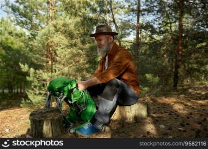 Cheerful senior male traveler preparing for rest after hiking in forest. Amazing adventure in woodland for retired people concept. Cheerful senior male traveler preparing for rest after hiking