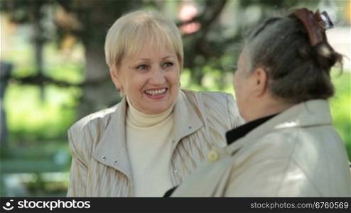 Cheerful senior woman speaks with female friend in the park