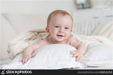 Cheerful smiling baby boy lying on big bed