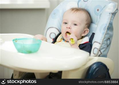 Cheerful smiling baby boy playing with spoon in highchair
