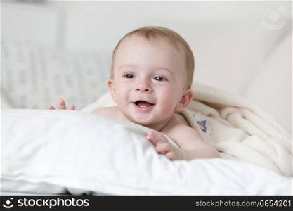 Cheerful smiling baby boy relaxing on big white pillow on bed
