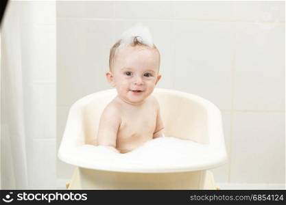 Cheerful smiling boy sitting in bath covered in foam
