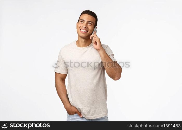Cheerful, smiling young man in t-shirt, having conversation with friend, looking up enthusiastic, hold hand in pocket casually, smartphone pressed to ear, talking joyfully, white background.. Cheerful, smiling young man in t-shirt, having conversation with friend, looking up enthusiastic, hold hand in pocket casually, smartphone pressed to ear, talking joyfully, white background