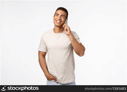 Cheerful, smiling young man in t-shirt, having conversation with friend, looking up enthusiastic, hold hand in pocket casually, smartphone pressed to ear, talking joyfully, white background.. Cheerful, smiling young man in t-shirt, having conversation with friend, looking up enthusiastic, hold hand in pocket casually, smartphone pressed to ear, talking joyfully, white background
