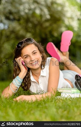Cheerful student girl lying on grass calling mobile phone summer