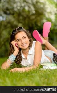 Cheerful student girl lying on grass calling mobile phone summer