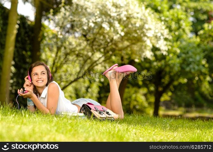 Cheerful student girl lying on grass listen music summer park