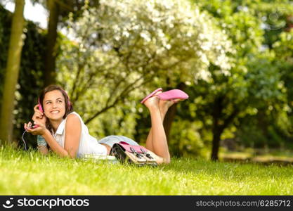 Cheerful student girl lying on grass listen music summer park