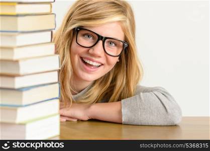 Cheerful student teenager looking from behind stack of books glasses