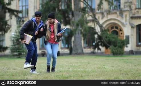 Cheerful students with books and tutorials dancing on campus lawn after passing exam. Students celebrating graduation from university dancing freestyle outdoors.