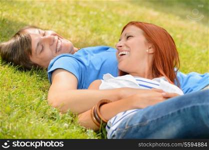 Cheerful teenage couple laughing at each other lying on grass