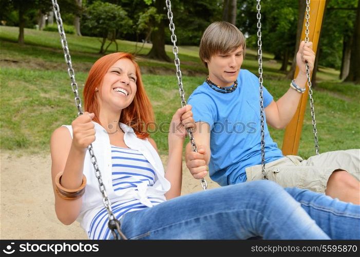 Cheerful teenage couple on swing in park girl laughing