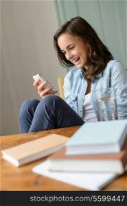 Cheerful teenage girl looking at mobile phone home read funny SMS