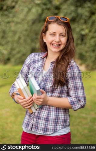 Cheerful teenage student with braces holding books at park