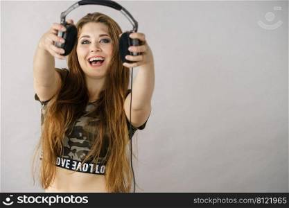 Cheerful teenage woman listening to music through big headphones having fun. Crazy girl. Teen women holding headphones