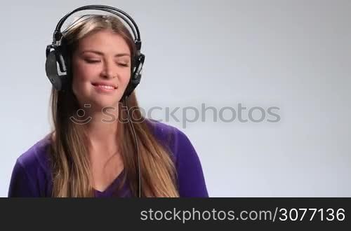 Cheerful teenager girl with headset listening to music on radio. Beautiful young brunette woman in earphones enjoying upbeat song, having fun, making funny facial expressions, gesturing, clicking her fingers in rhythm and moving groovily to the beat.