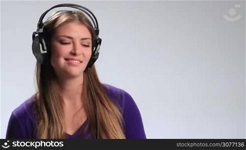 Cheerful teenager girl with headset listening to music on radio. Beautiful young brunette woman in earphones enjoying upbeat song, having fun, making funny facial expressions, gesturing, clicking her fingers in rhythm and moving groovily to the beat.