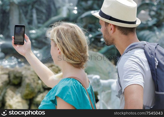 cheerful traveling couple taking pictures with mobile phone