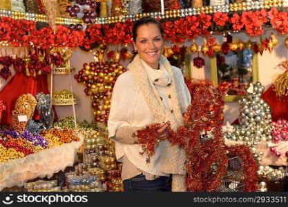 Cheerful woman customer buying Christmas tinsel garland in decoration shop