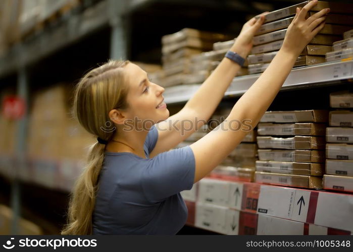 Cheerful woman customer looking up and pulling product on shelf while shopping in hardware store