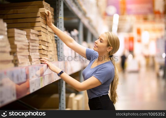 Cheerful woman customer looking up and pulling product on shelf while shopping in hardware store