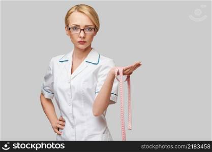 Cheerful woman doctor or nurse holding a measure tape standing over grey background.. Cheerful woman doctor or nurse holding a measure tape standing over grey background