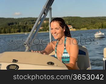 Cheerful woman in bikini navigating powerboat in summer