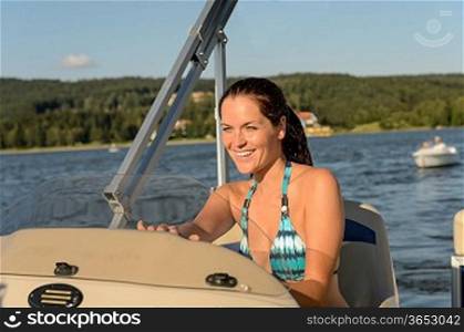 Cheerful woman in bikini navigating powerboat in summer