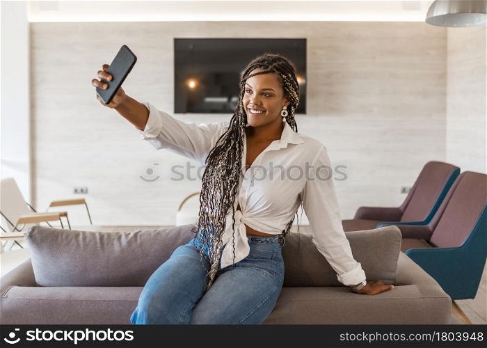 Cheerful woman in her home using phone yo take a selfie. African American woman with braids inside of home taking a selfie.. Cheerful woman in her home using phone yo take a selfie
