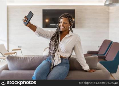 Cheerful woman in her home using phone yo take a selfie. African American woman with braids inside of home taking a selfie.. Cheerful woman in her home using phone yo take a selfie