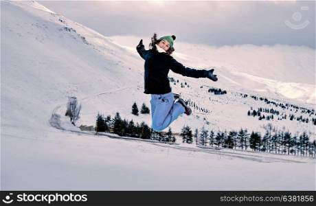 Cheerful woman jumping in the mountains covered with snow, spending winter holidays on the ski resort, enjoying winter vacation, happy active lifestyle