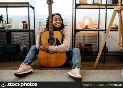 Cheerful woman sitting on the floor and hugs the guitar at home. Pretty lady with musical instrument relax in the room, female music lover resting. Woman sitting on the floor and hugs the guitar